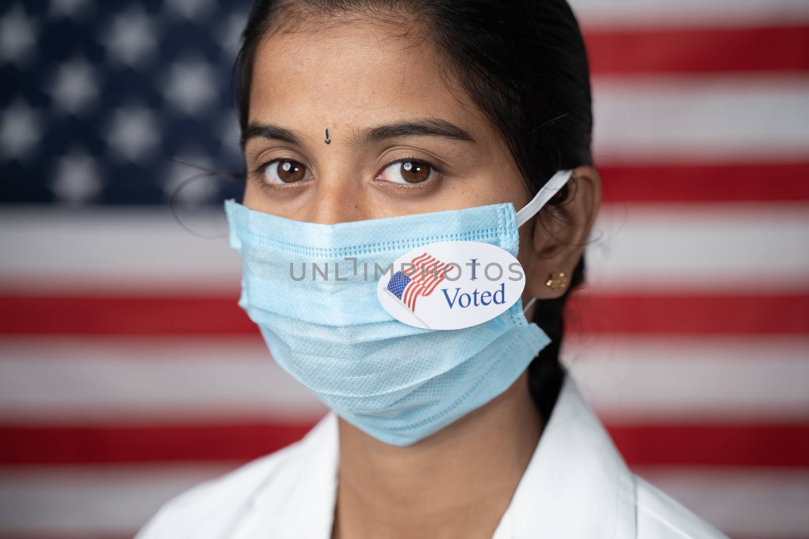 Girl with I voted sticker on medical face mask with US flag as background - concept of US election