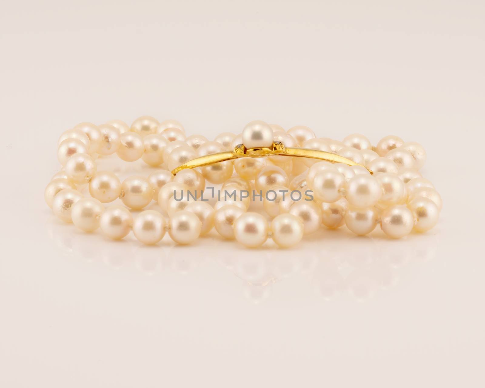 A string of lustrously glowing natural pearls designed as a necklace with a yellow gold bar center feature adorned with a pearl, isolated on a white background