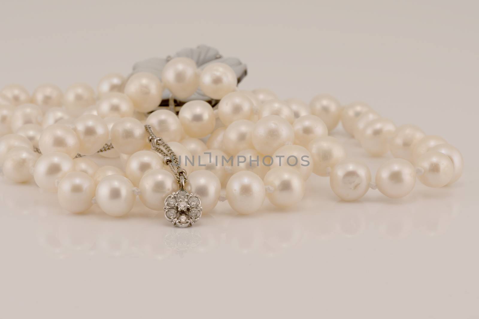 A flower design diamond and white gold pendant nestled in front of lustrous pearls, isolated on a white background