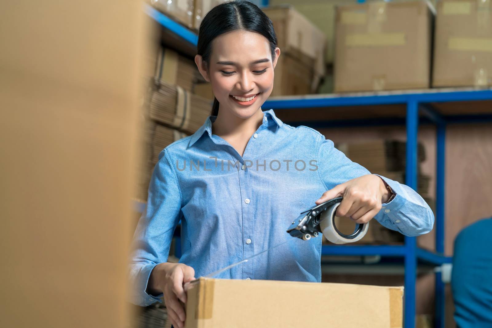 Portrait of Warehouse worker woman packing cardboard box with st by Tzido