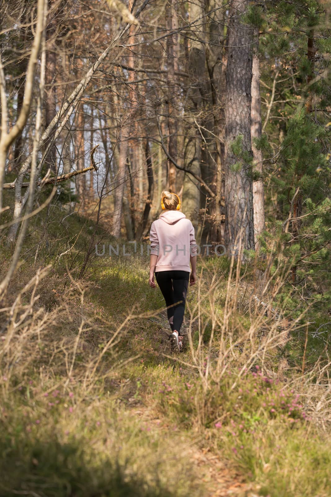 Rear view of active sporty woman listening to the music while running in autumn fall forest. Female runner training outdoor. Healthy lifestyle image of young caucasian woman jogging outside by kasto