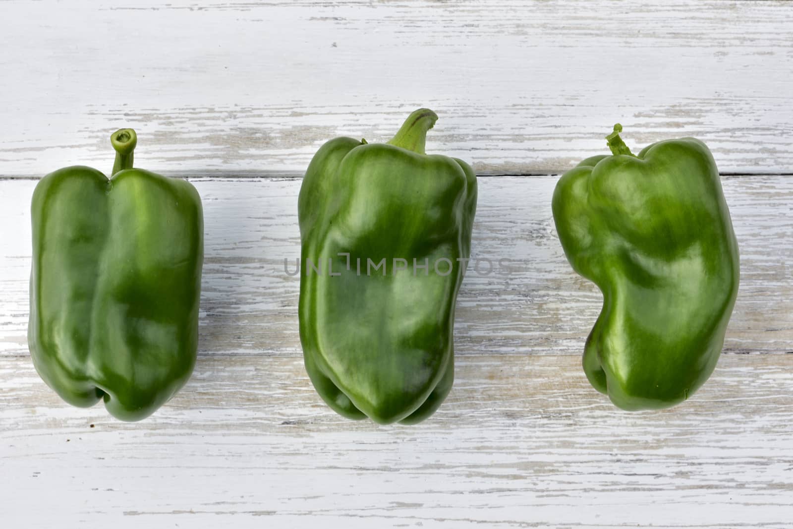 three pods of green bell peppers on a wooden vintage table, top view