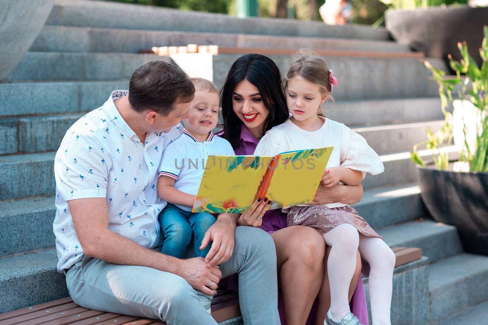 Happy young family with two kids sitting in the park reading a book. Happy parenting concept