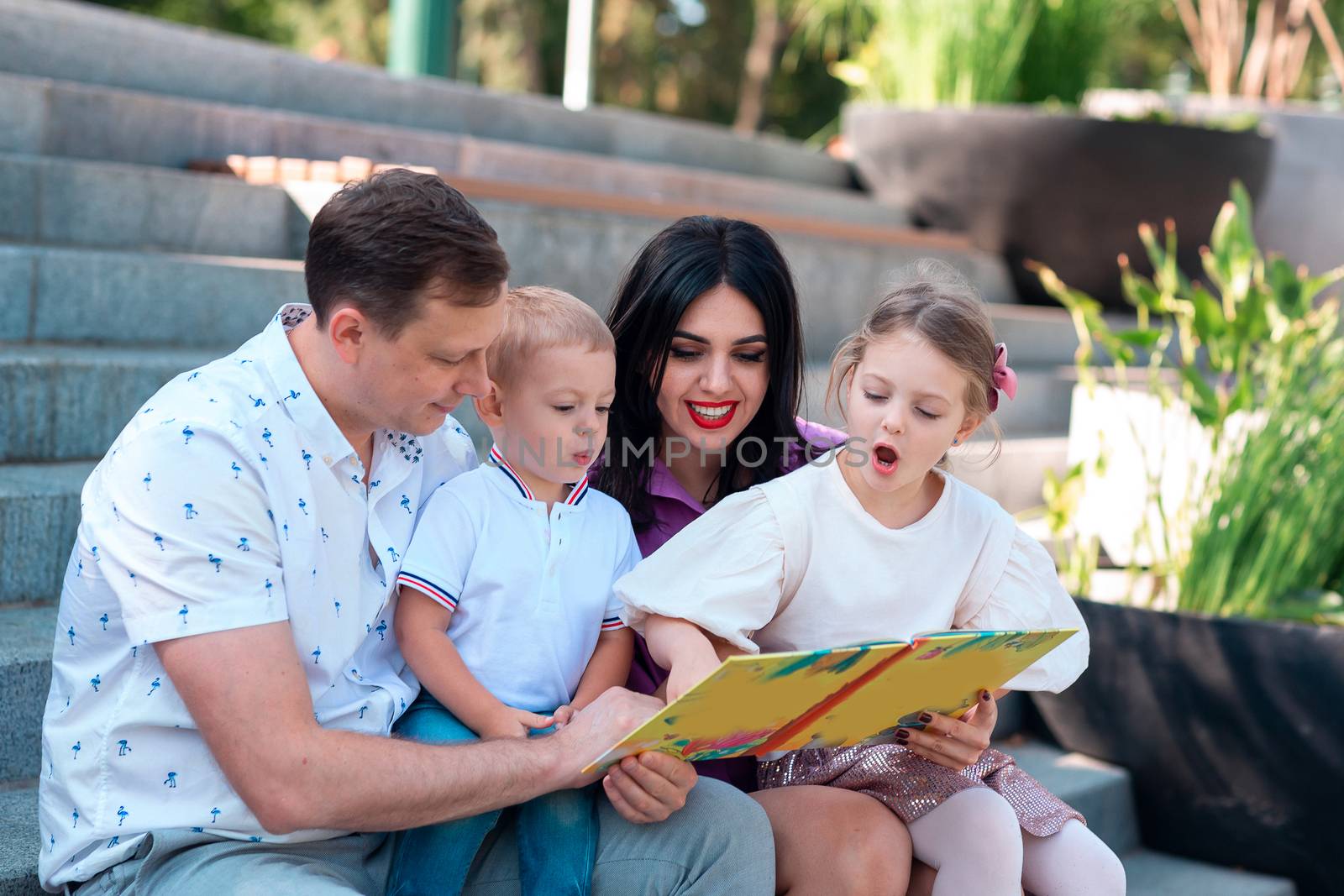 Happy young family with two kids sitting in the park reading a book. Happy parenting concept