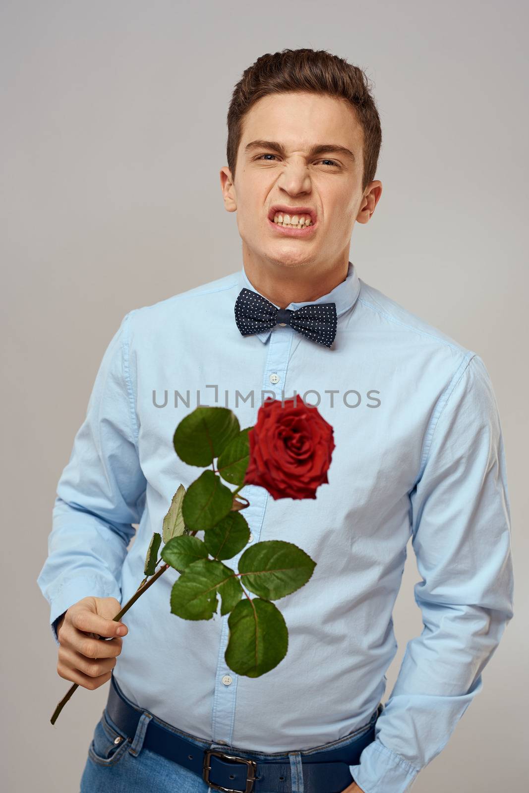 Romantic man with a red rose and in a blue shirt with a bow tie around his neck gray background. High quality photo