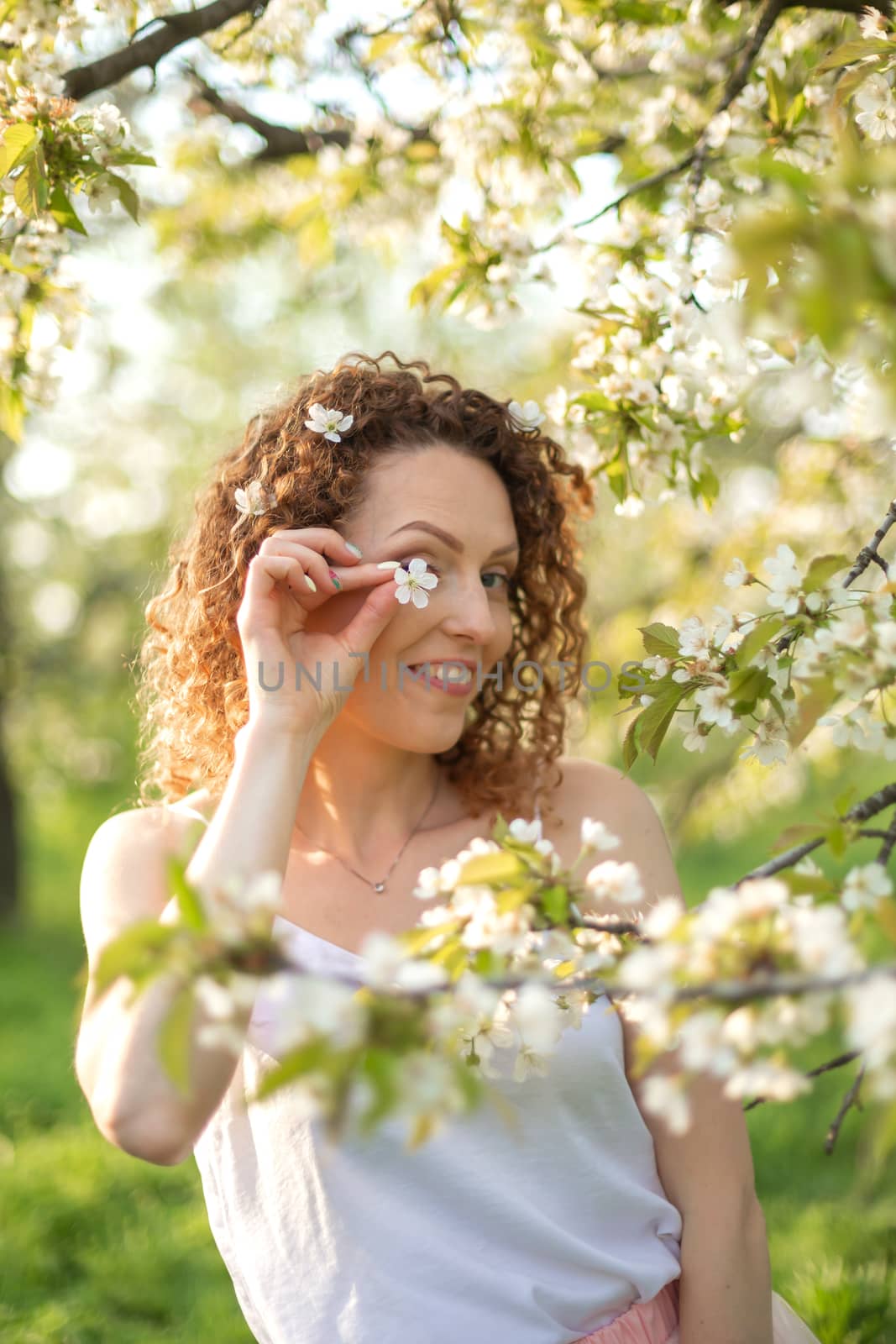 Young attractive girl walks in spring green park enjoying flowering nature. Healthy smiling girl spinning on the spring lawn. Allergy without.