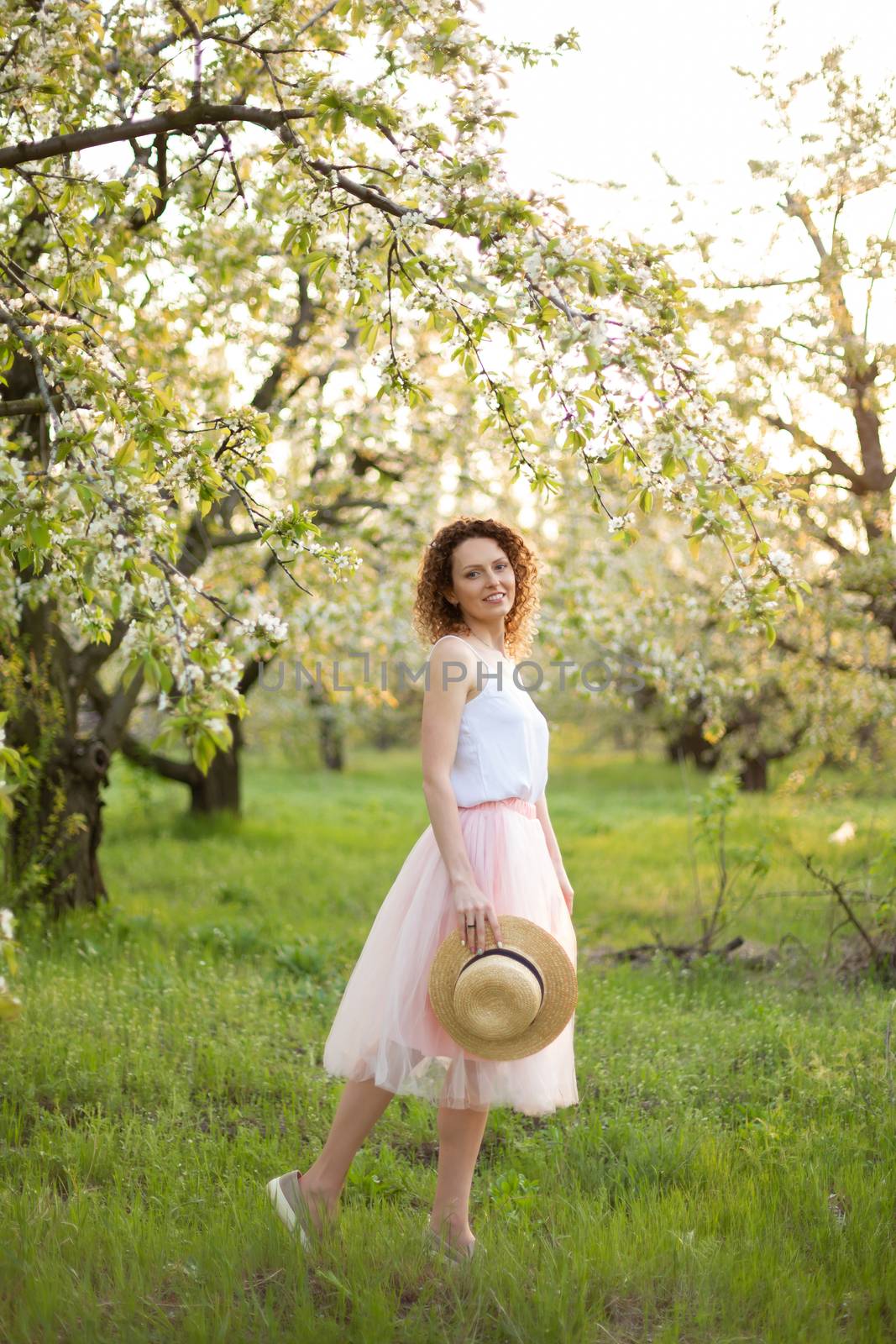 Young attractive woman with curly hair walking in a green flowered garden. Spring mood.