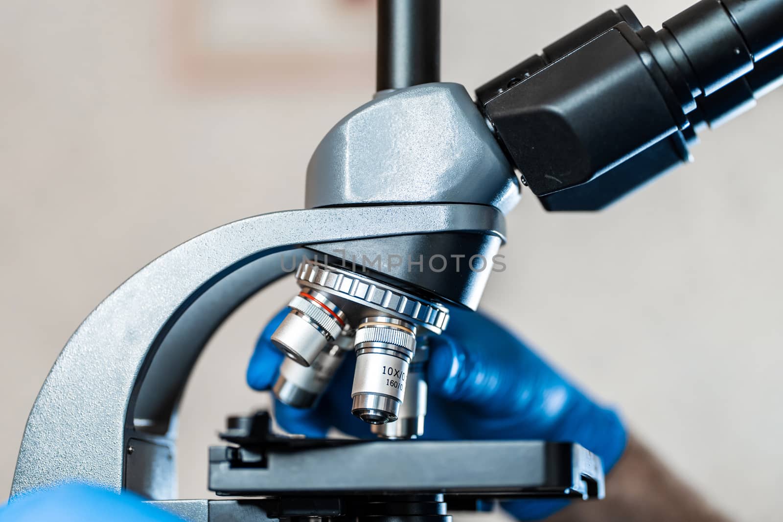 Male laboratory assistant examining biomaterial samples in a microscope. Cllose up hands in blue rubber gloves adjust microscope.