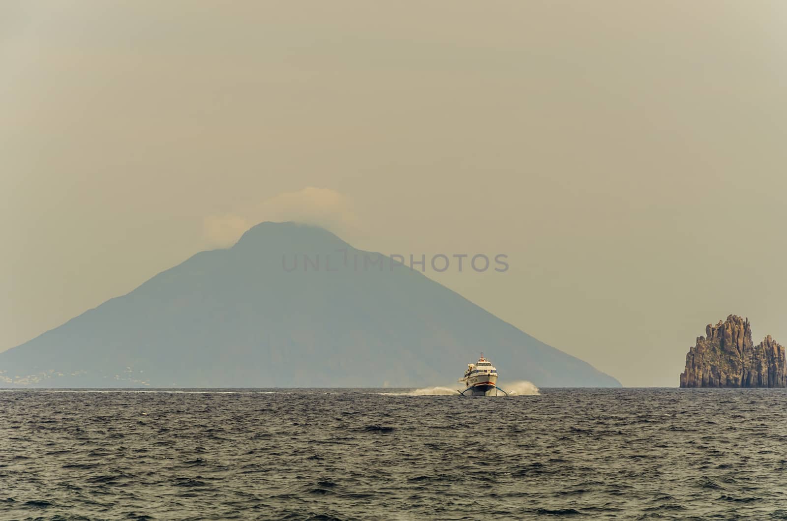 Sea tyrrhenian  boat catamaran rock volcanic emerging from the sea and in the background volcano stromboli smoking from the island panarea