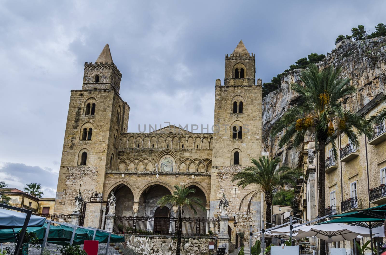 main church of cefalu with its particular architectural style buildings of the city and the famous rock formation of the city behind the church