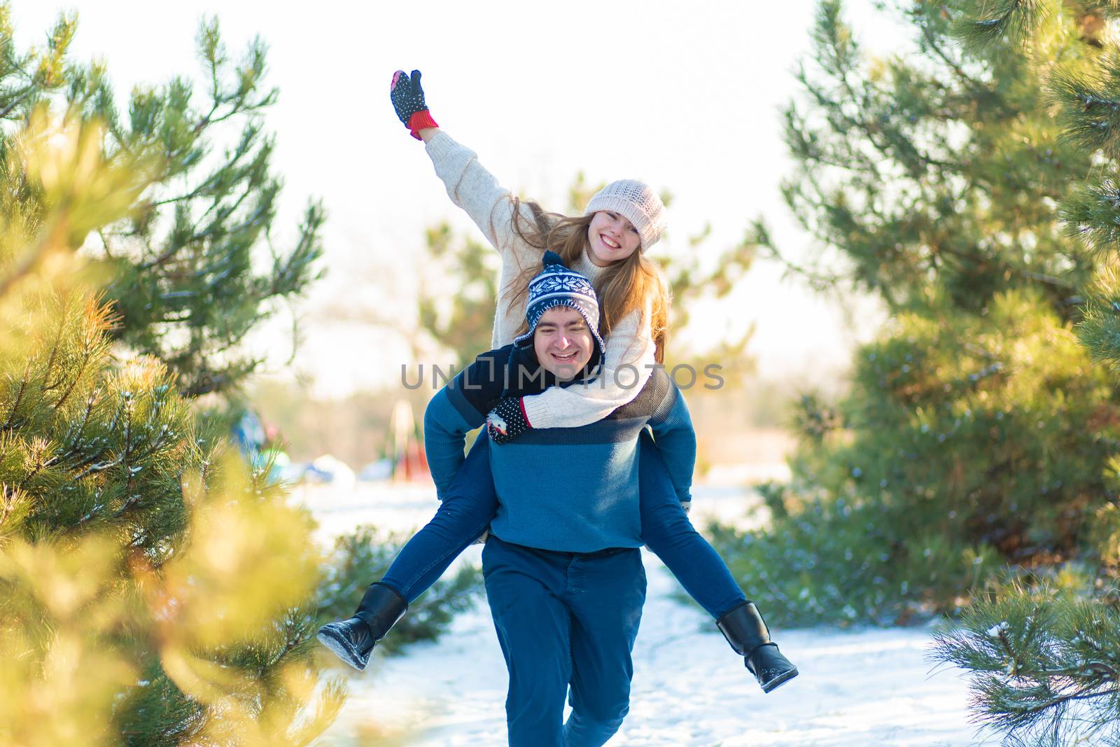 Loving couple play in the winter in the forest. Girl rides a guy in the background of the Christmas tree. Laugh and have a good time.