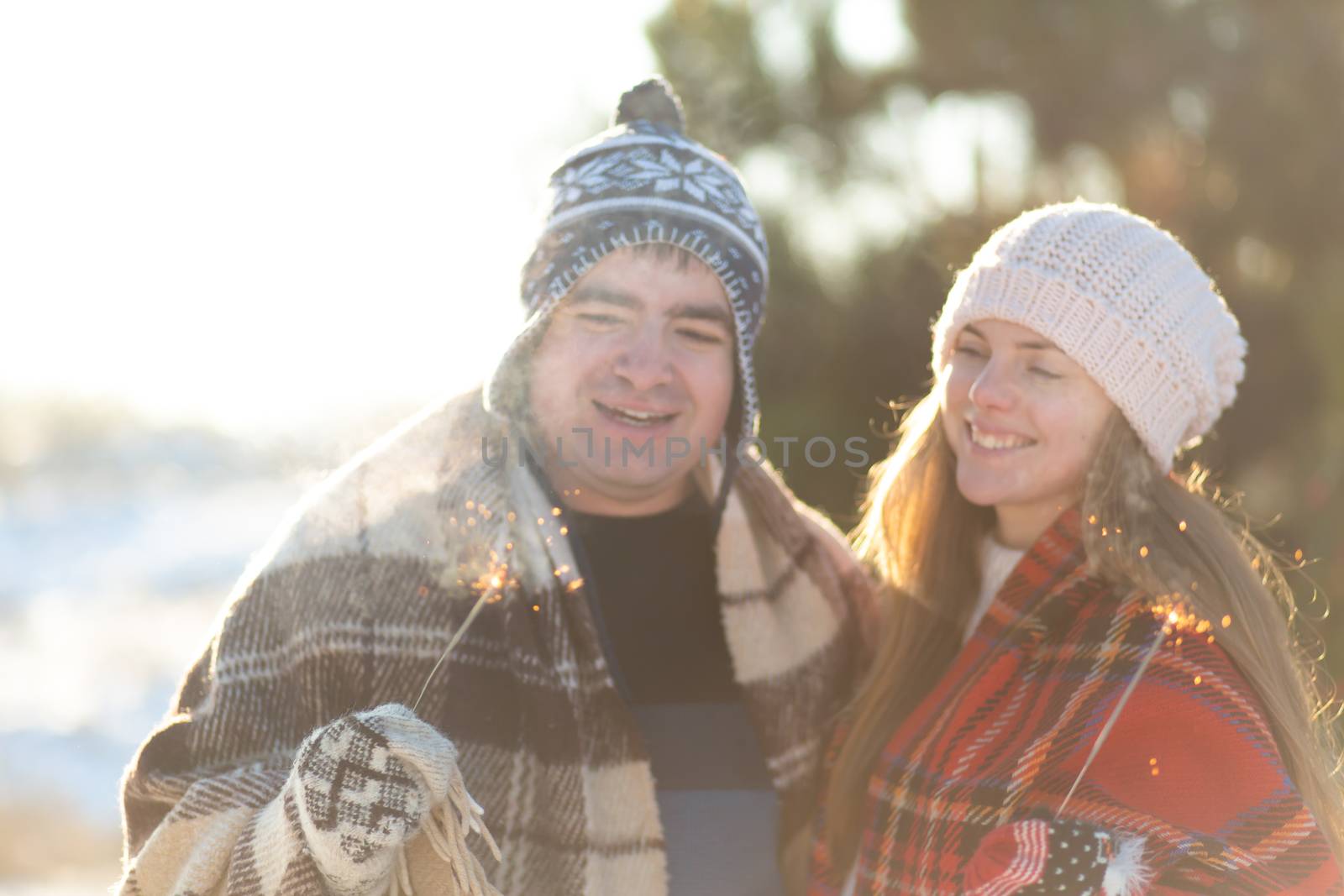 A loving couple in warm plaids kisses holding sparklers in their hands. Meet the winter holidays in a snowy forest.