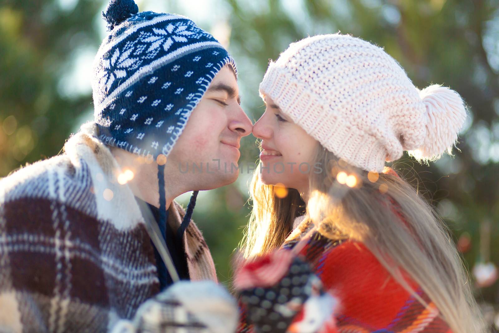 A loving couple in warm plaids kisses holding sparklers in their hands. Meet the winter holidays in a snowy forest.