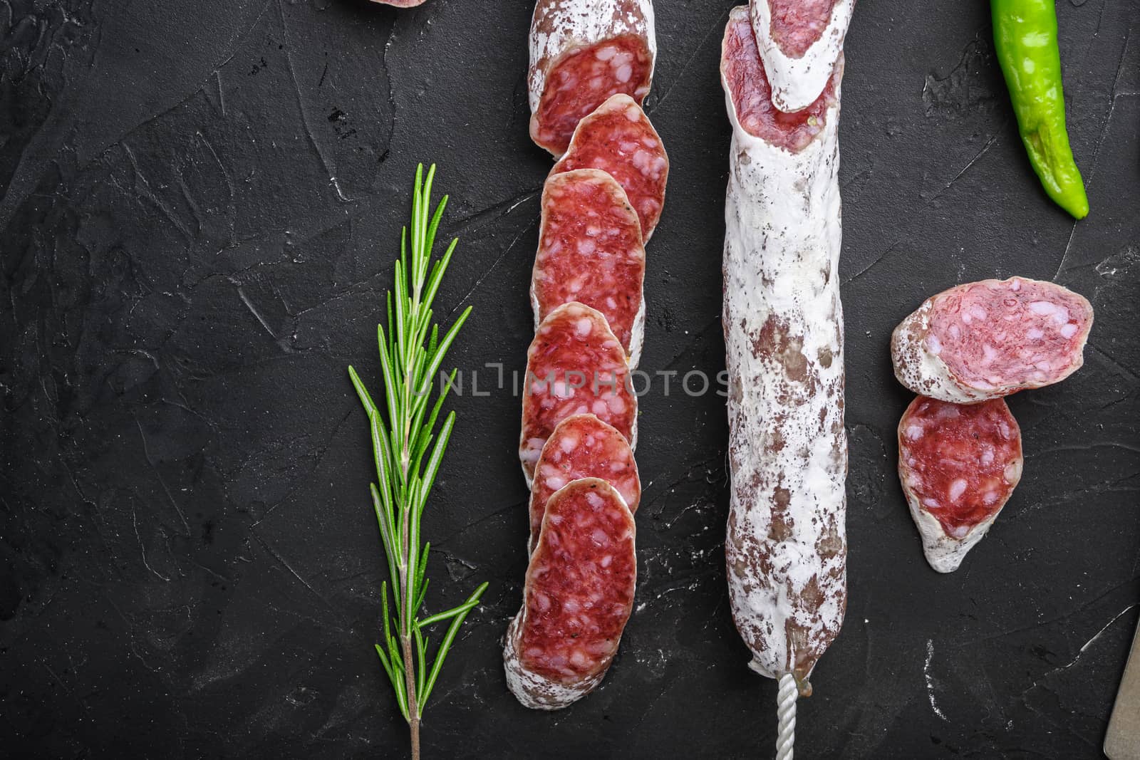 Dry cured fuet salami sausage slices on balck background, top view with copy space.