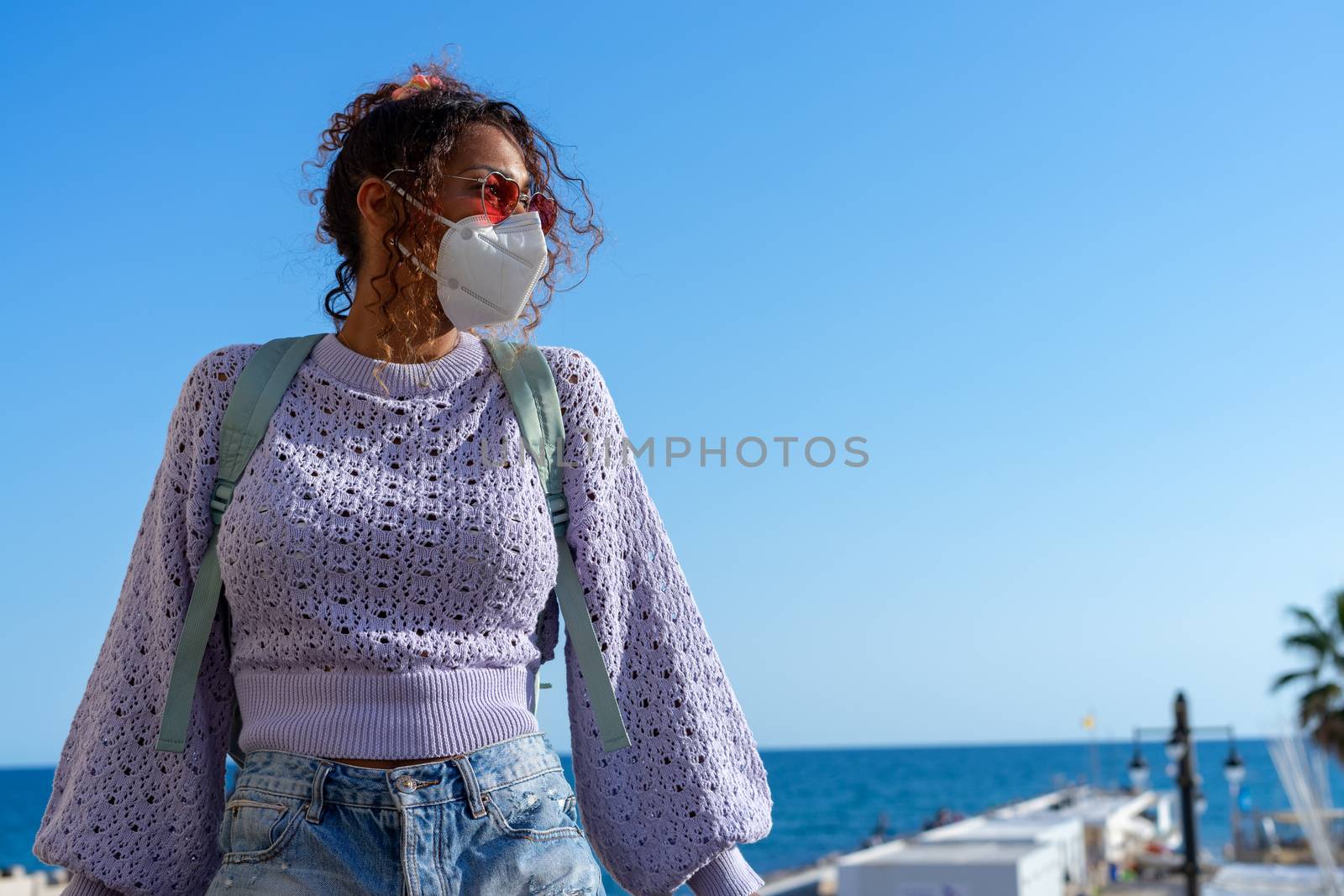 Portrait of an attractive young black woman walking with backpack and mask. Sightseeing