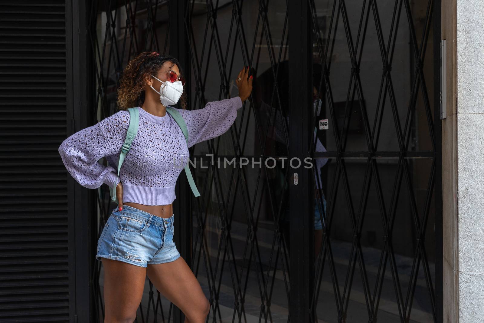 Young pretty black woman waiting to enter home with mask on the street.