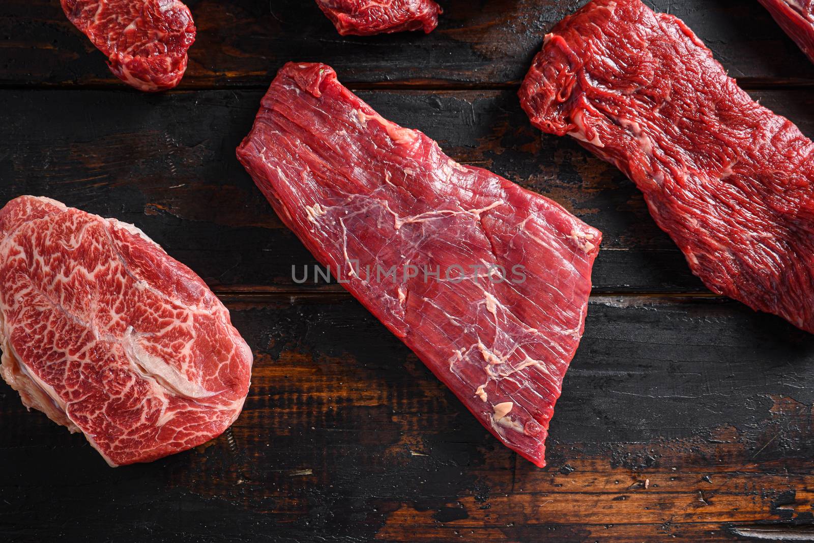 Bio Flank bavette or flap steak beef t steak near tri-tip and top blade oyster cuts close up in front of other cuts in butchery on old wood table top view.