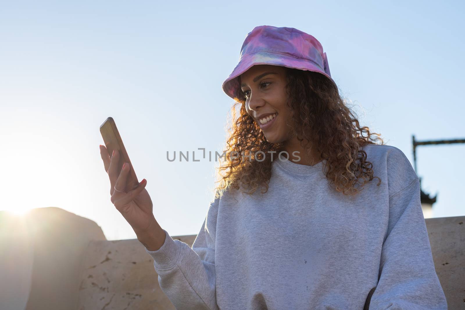 Portrait of an attractive young black woman sitting and talking with the mobile phone outdoors with her mask off. Concept communication