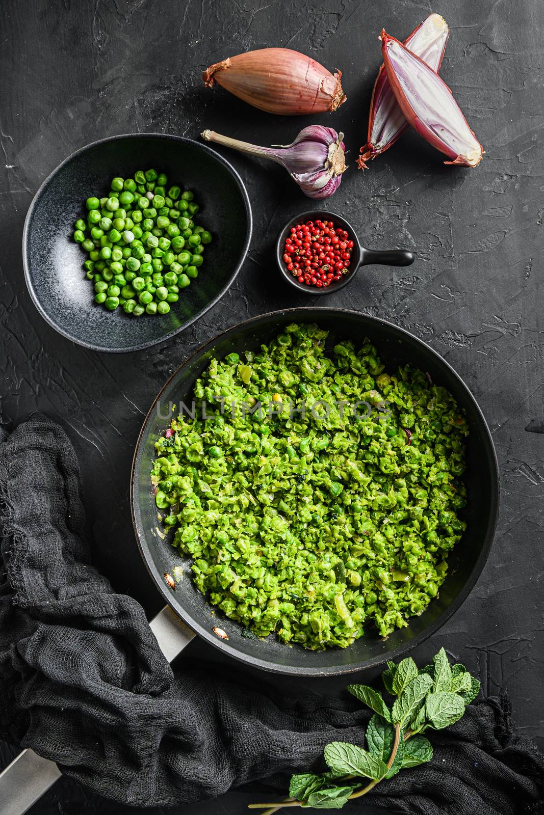 Mushy peas recipe cooked frying pan and peas in bowl with mint shallot pepper and salt over black stone surface top view organic keto food flat lay overhead photo.
