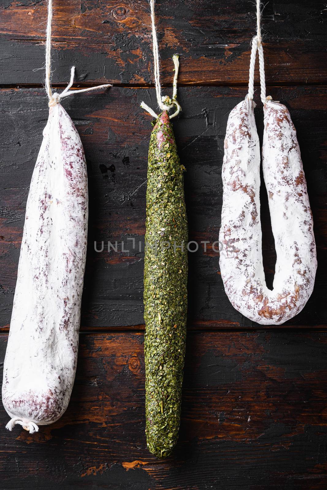 Spanish dry sausages hang from a rack at market on dark wood background.