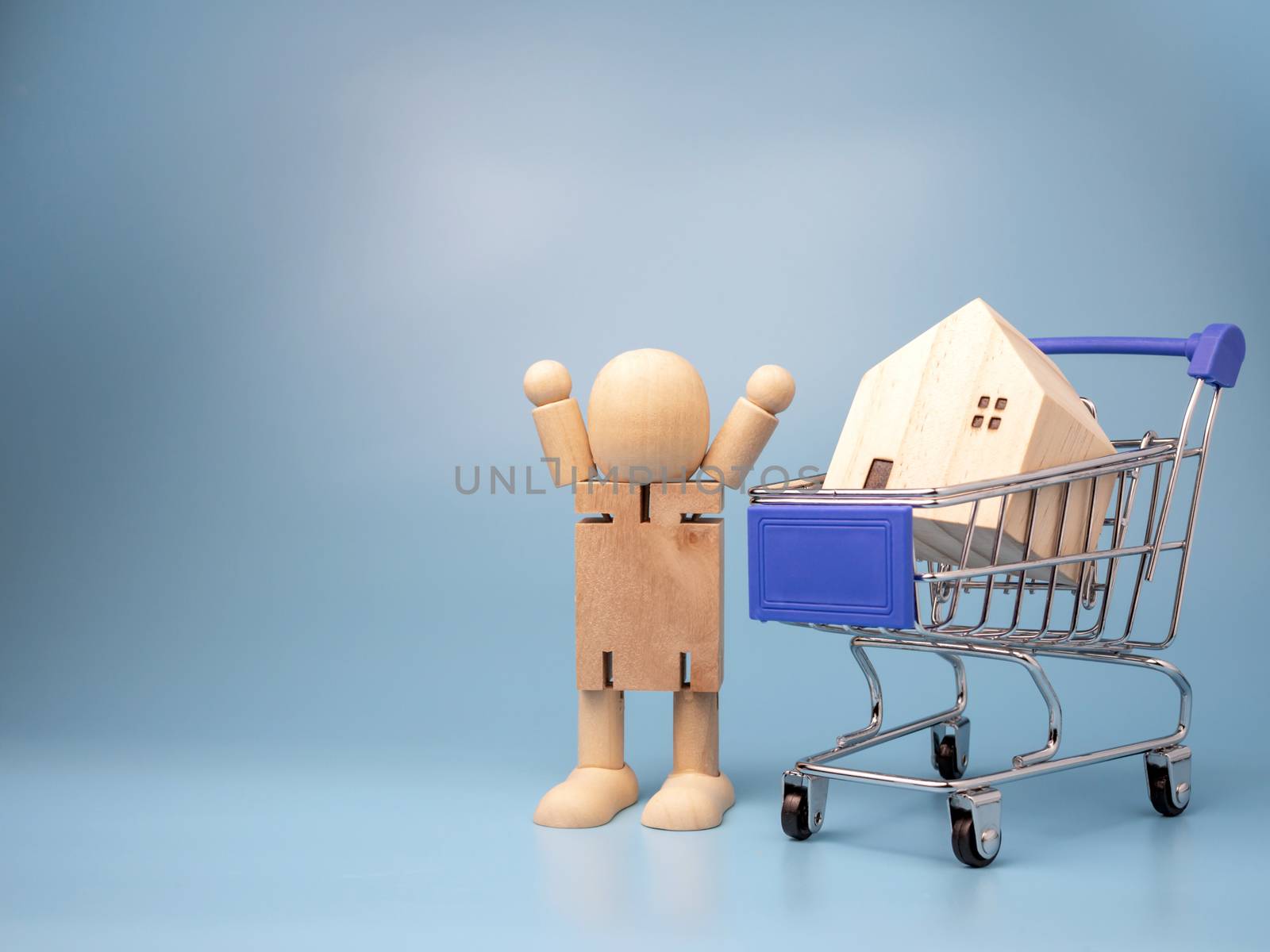 Wooden dolls that Stand next to the shopping cart With a model wooden house on top And has a blue background. Home buying and selling ideas