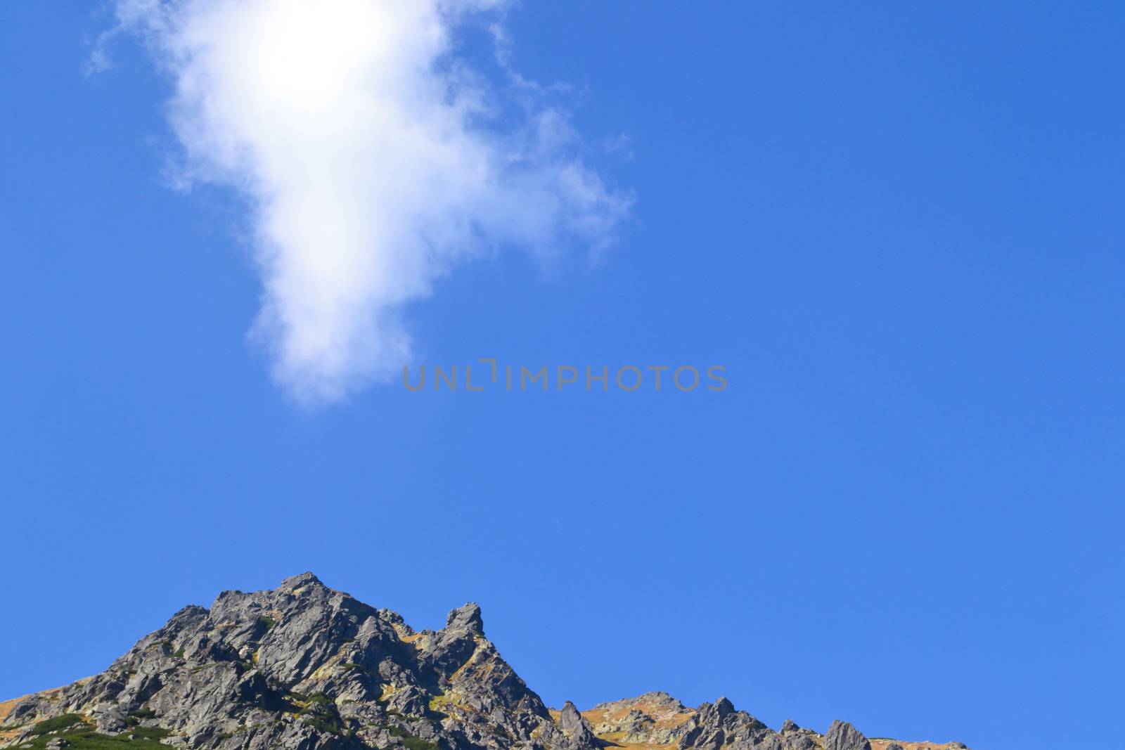 A cloud against a blue sky hovered over the top of the mountain. Background to illustrate heights or maximum possible achievements