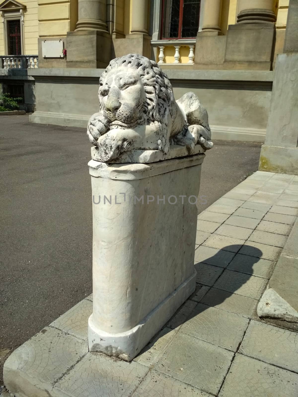 statue of a stone lion sleeping on a pedestal in front of an old mansion