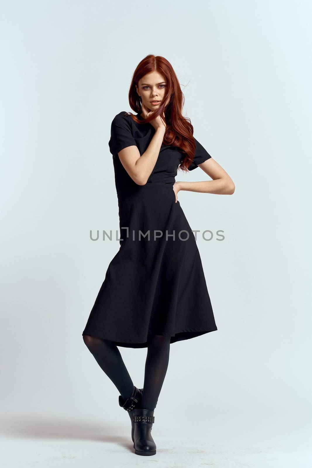 A woman in a black dress on a light background and pantyhose shoes red hair and pose in full growth by SHOTPRIME