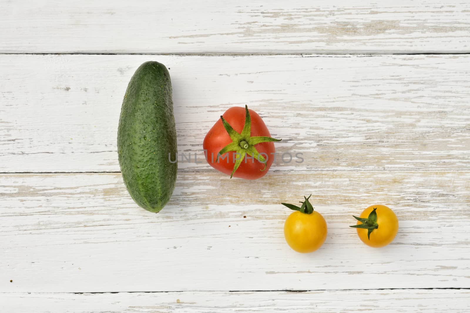 red tomato, two yellow small tomatoes and a cucumber on a wooden vintage table, top view