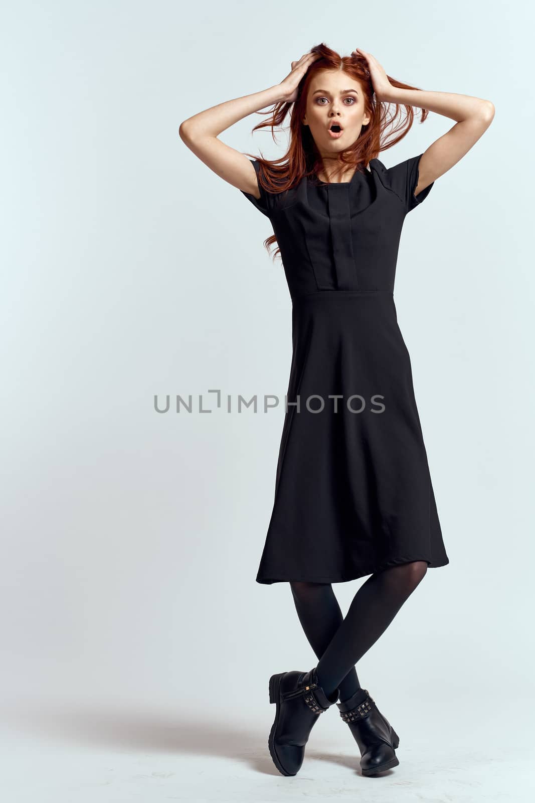 A woman in a black dress on a light background and pantyhose shoes red hair and pose in full growth. High quality photo