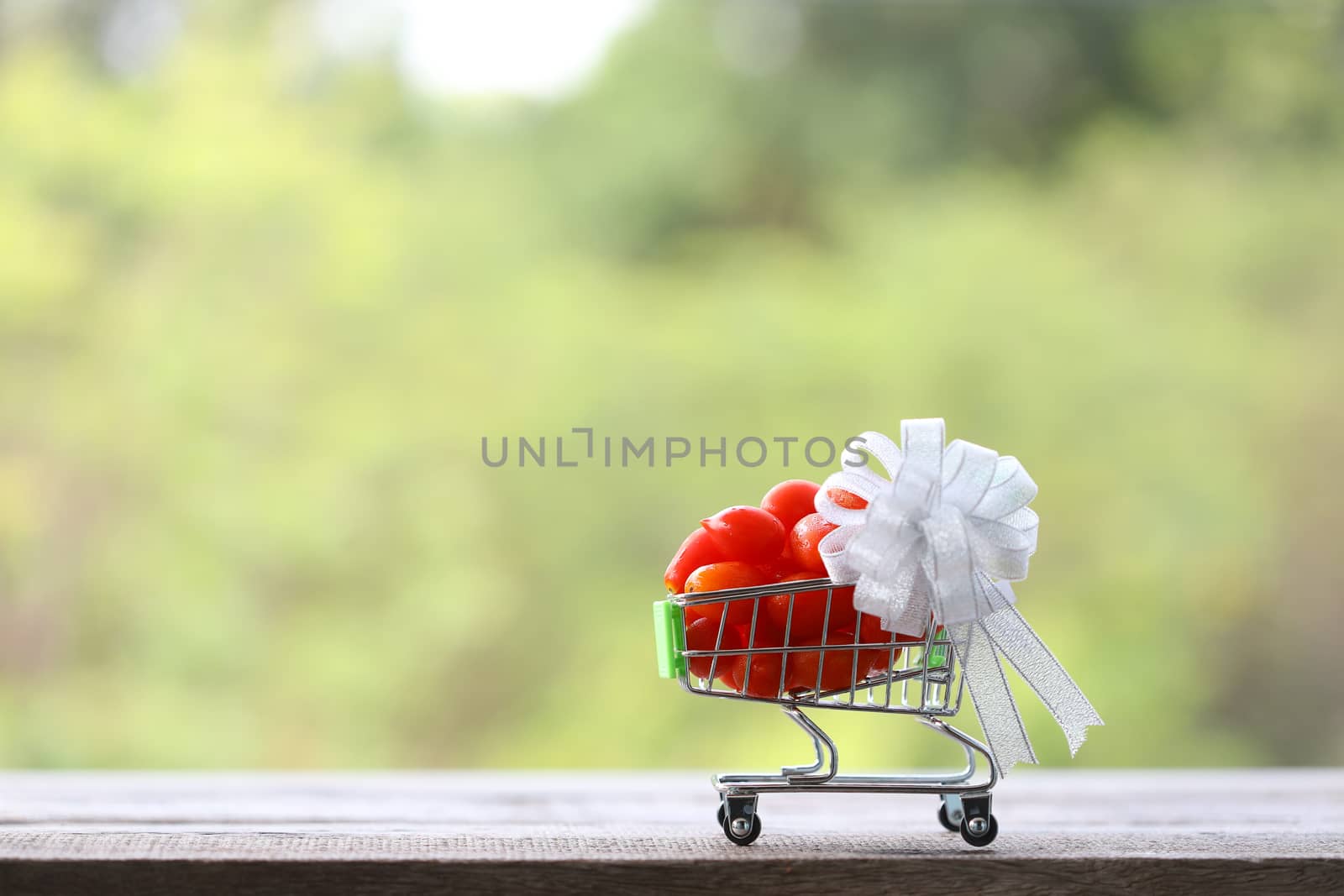 small Tomatoes in mini shopping basket with white ribbon on wooden table
