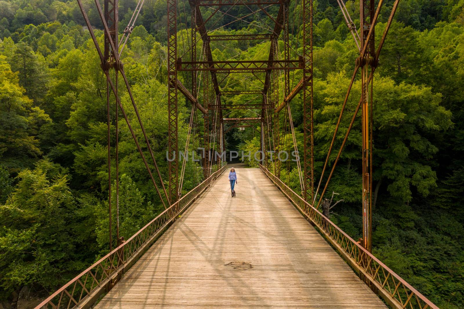 Aerial view of a senior woman walking her dog across the historic metal truss Jenkinsburg Bridge near Morgantown over Cheat River