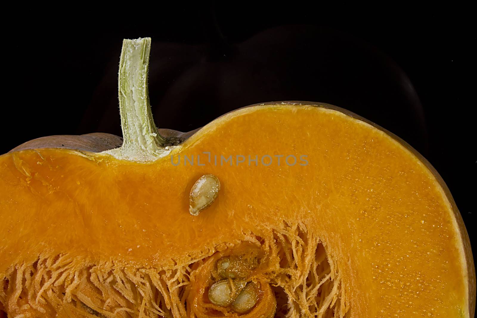 Cut ripe orange pumpkin close up on black background