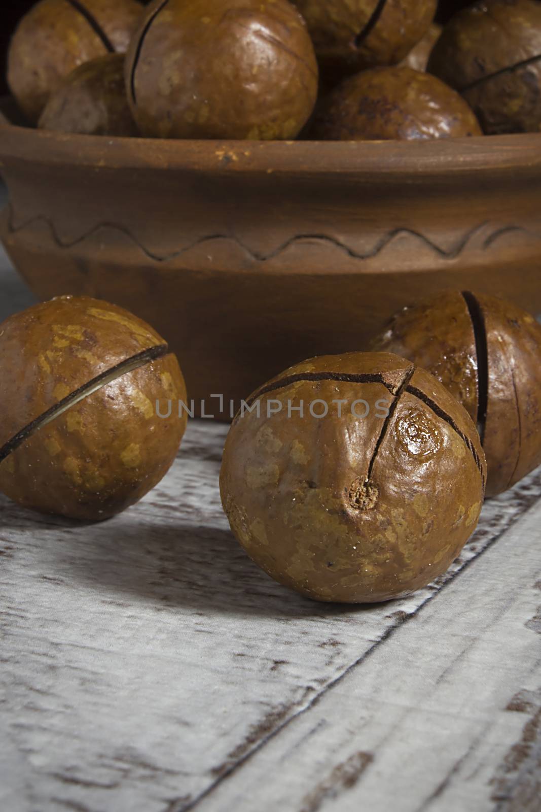 Macadamia nuts in shells in earthenware dish on wooden table