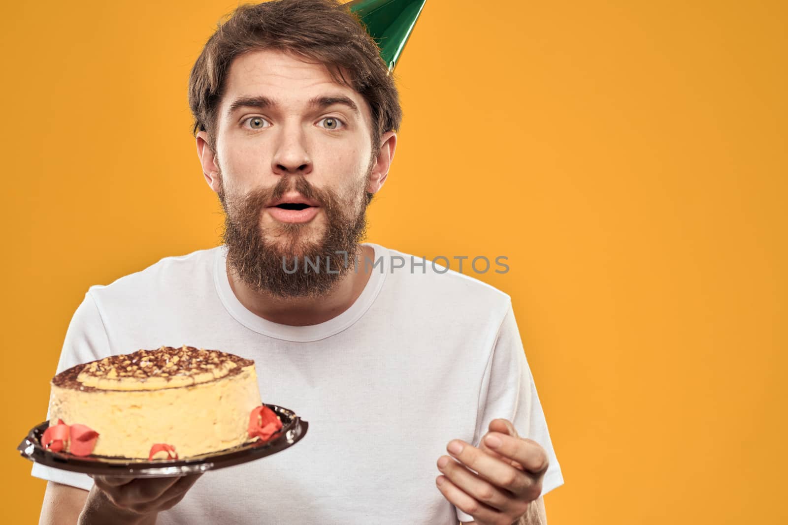 Handsome man with a beard and in a cap celebrating a birthday party yellow background. High quality photo