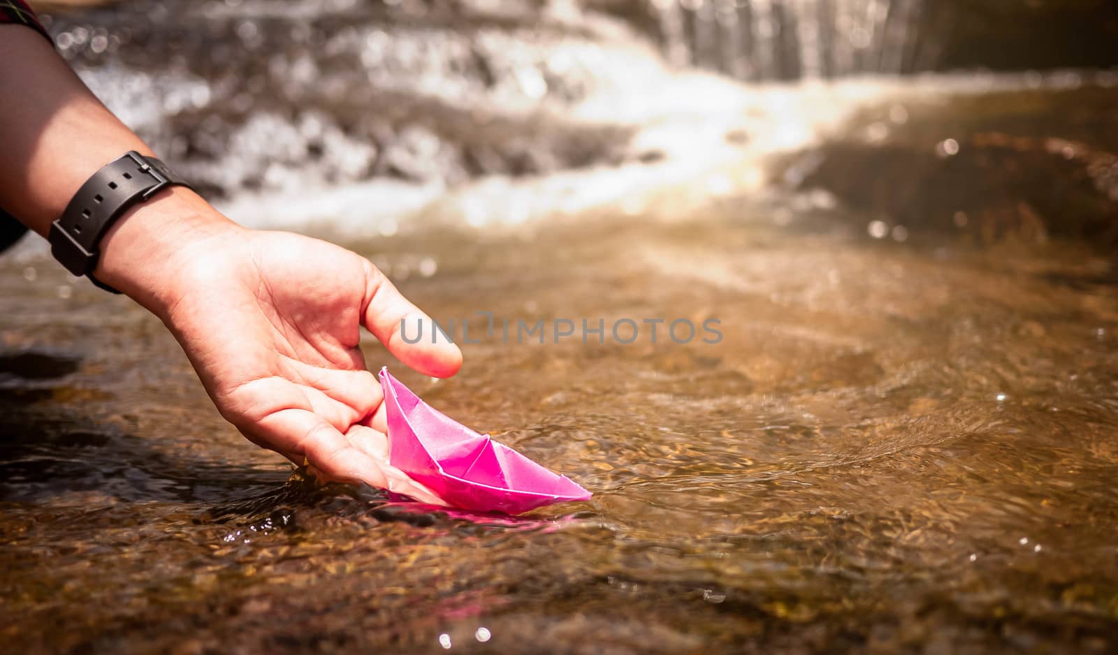 Close up of Woman's hand putting paper boat on the water and pus by TEERASAK