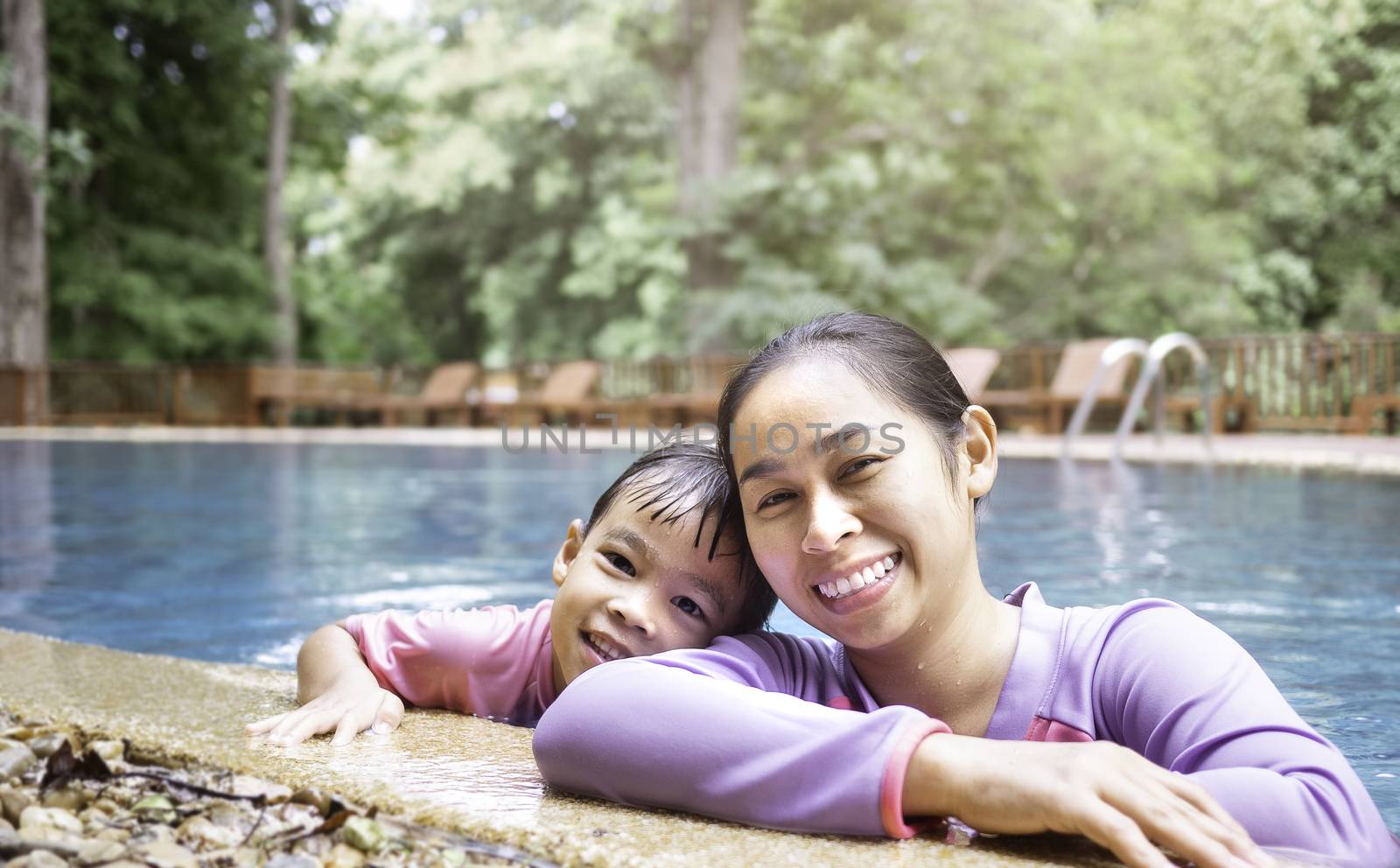 Happy young mother and her daughter smiling in swimming pool in a hot summer day. Family lifestyle in vacation.