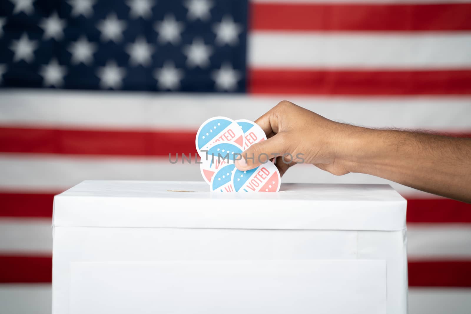 Close up of Hands dropping multiple I Voted sticker inside Ballot box with US flag as background, Concept of fraud in USA elections. by lakshmiprasad.maski@gmai.com