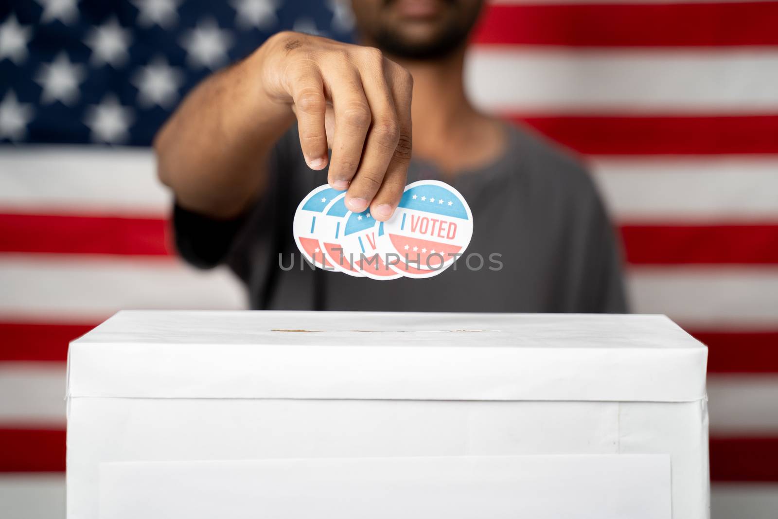 Close up of Hands dropping multiple I Voted sticker inside Ballot box with US flag as background, Concept of fraud in USA elections