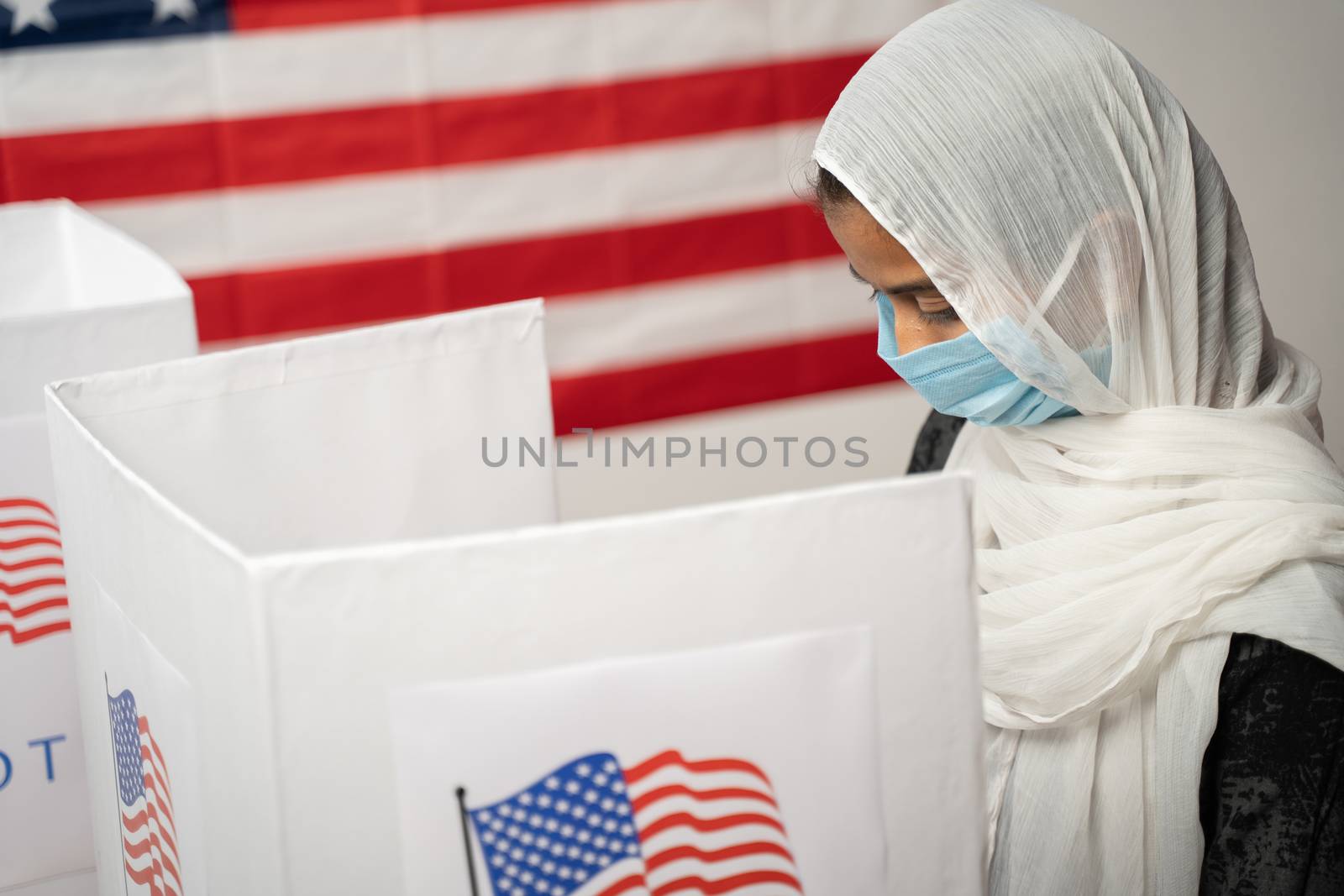 Girl with Hijab or head covering and mask worn busy at polling booth with US flag as background - Concept of US election. by lakshmiprasad.maski@gmai.com