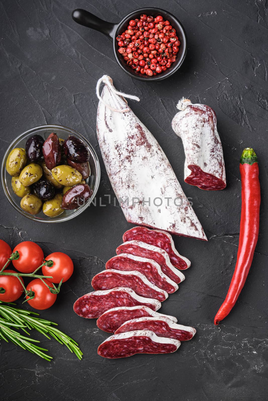 Spanish longaniza salami sausage slices with herbs on black textured background, topview.