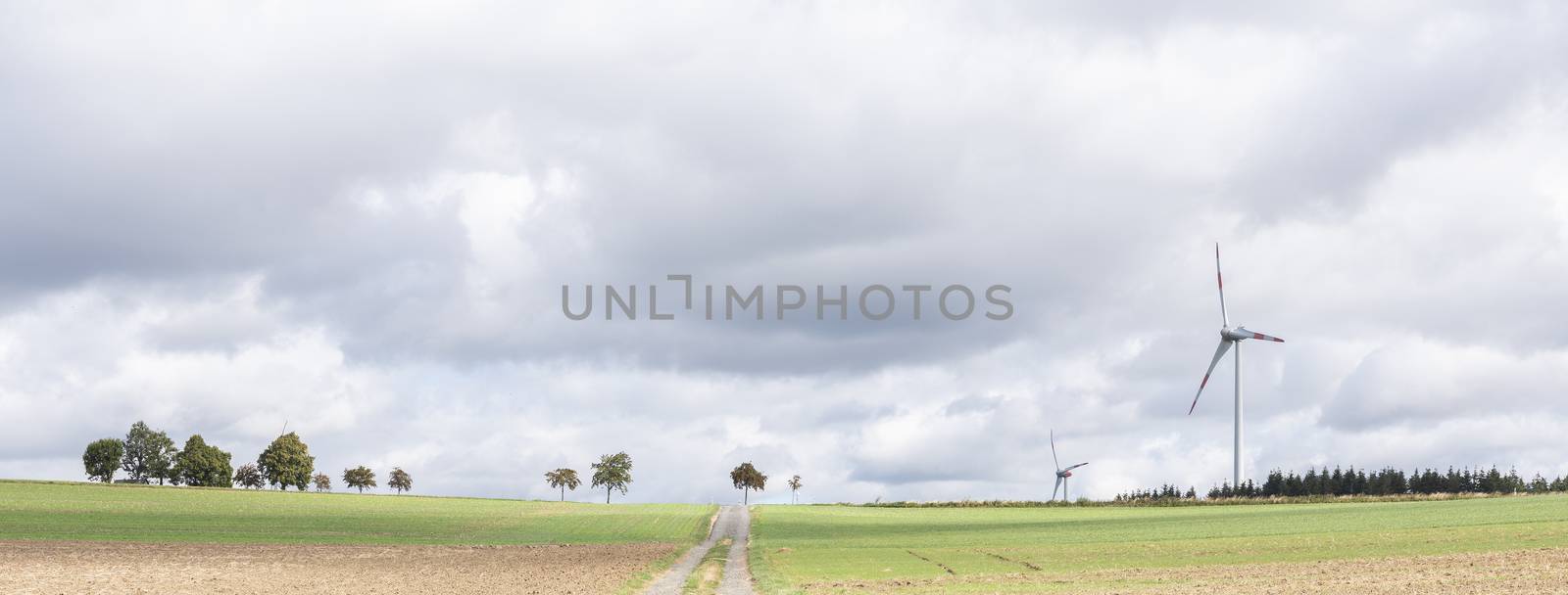 empty country road between fields on high plane neer Cochem in german eifel under cloudy sky in summer with wind turbines