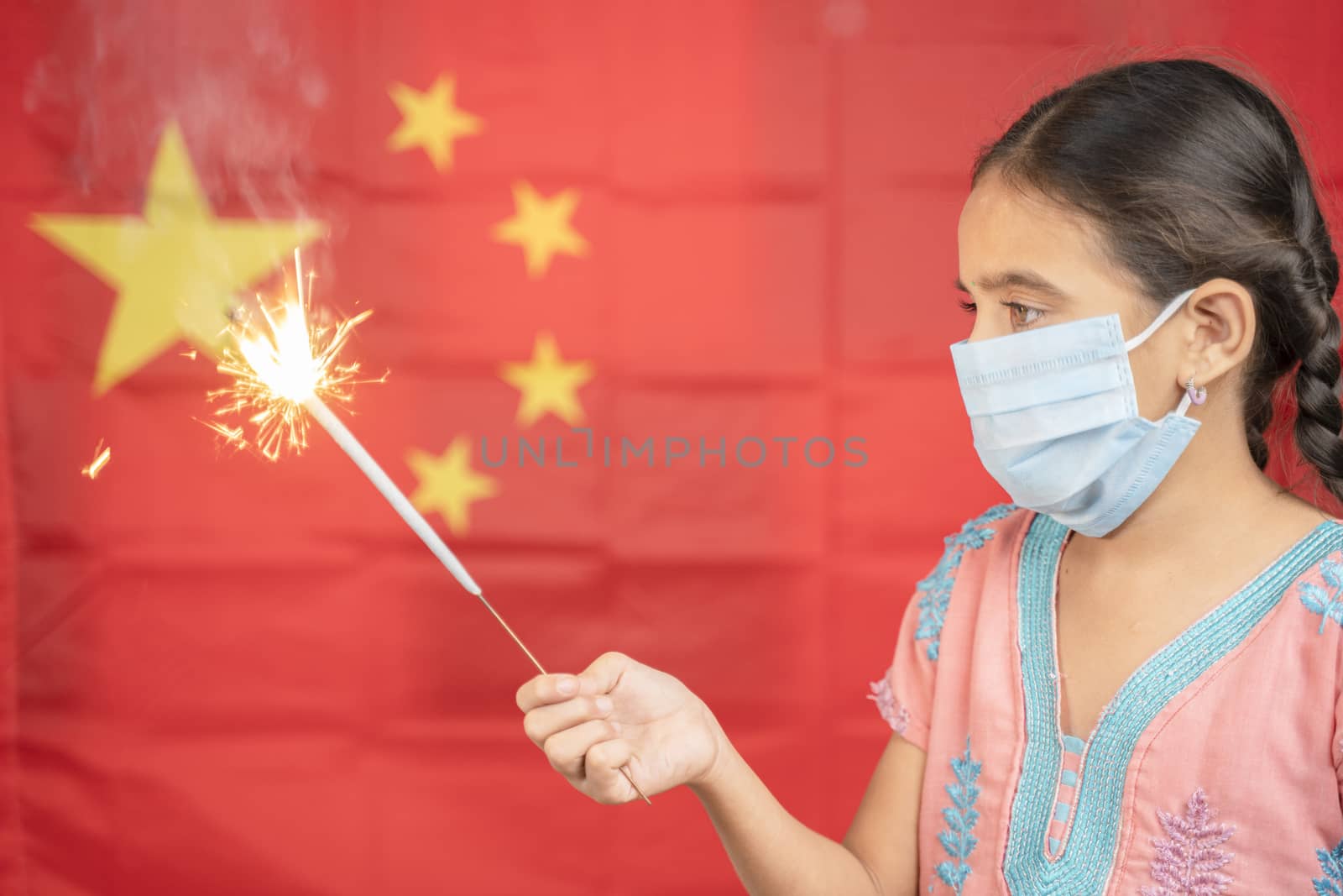 Young Girl Kid on medical mask holding Sparkler with Chinese flag as background - concept showing Celebration of Chinas National or Republic Day.