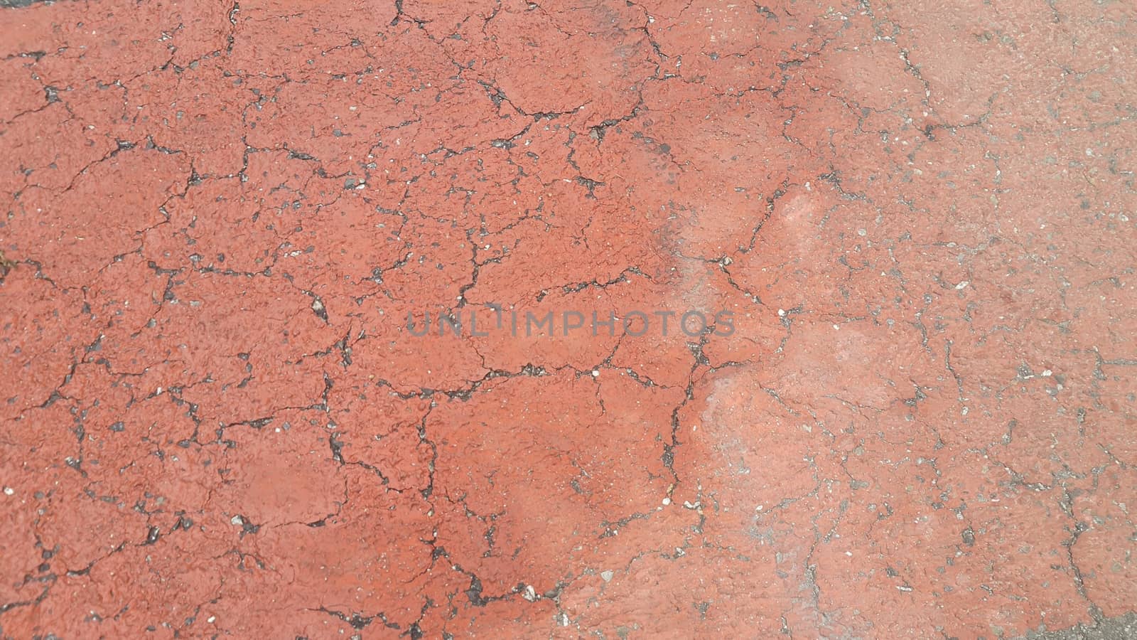 Red colored damaged road or paved pathway with crackes of different shpaes. Cracked texture with copy space for text and messages