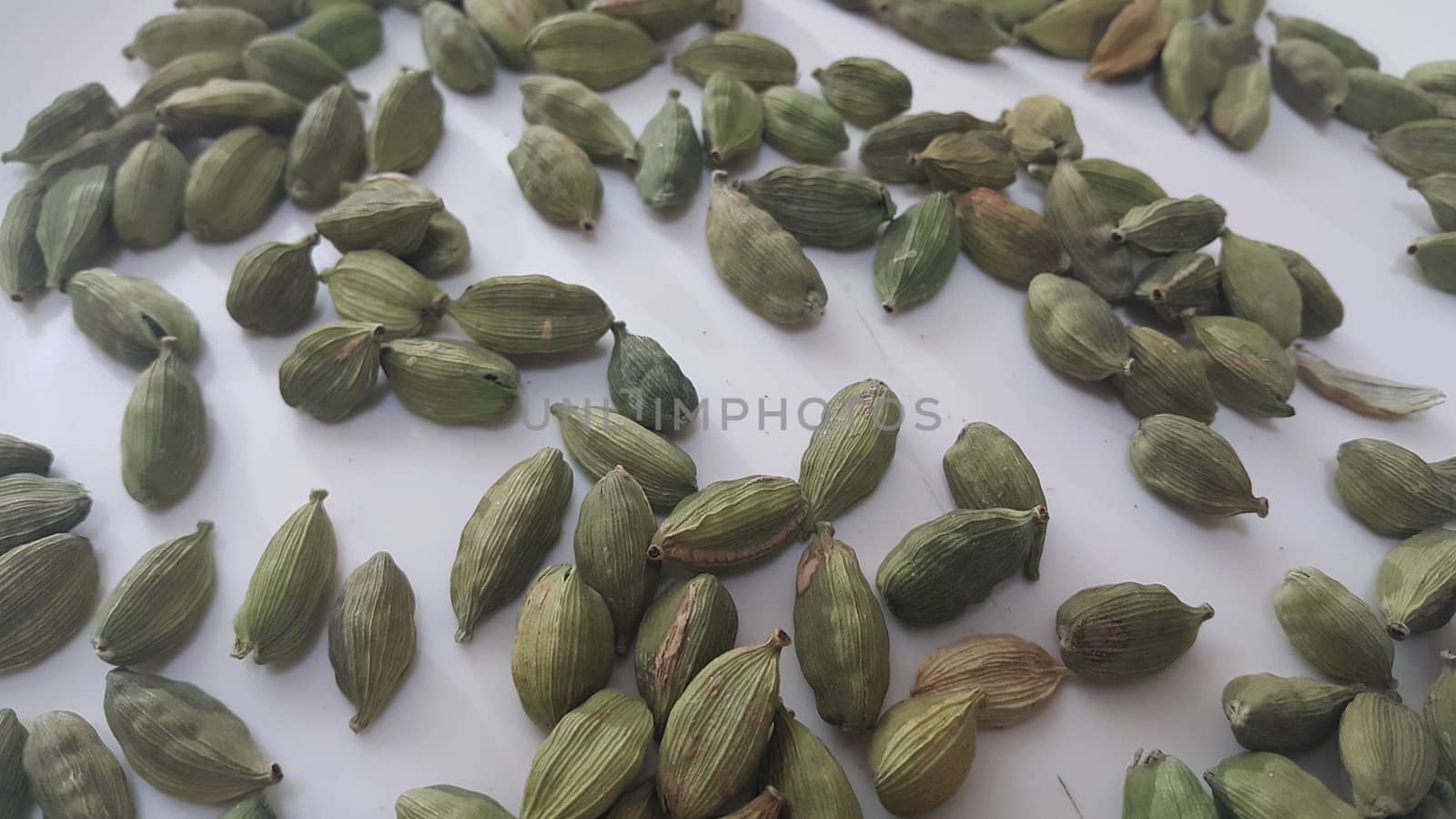 Closeup top view of dried green Elettaria cardamomum fruits with seeds, cardamom spice scattered on white background