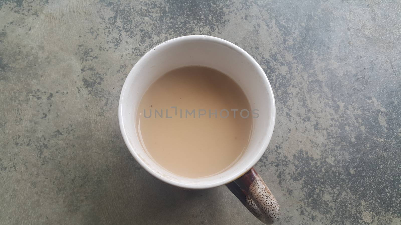 Beautiful coffee white mug with black milk-tea over concrete grey floor. A top view of tea cup filled with tea.