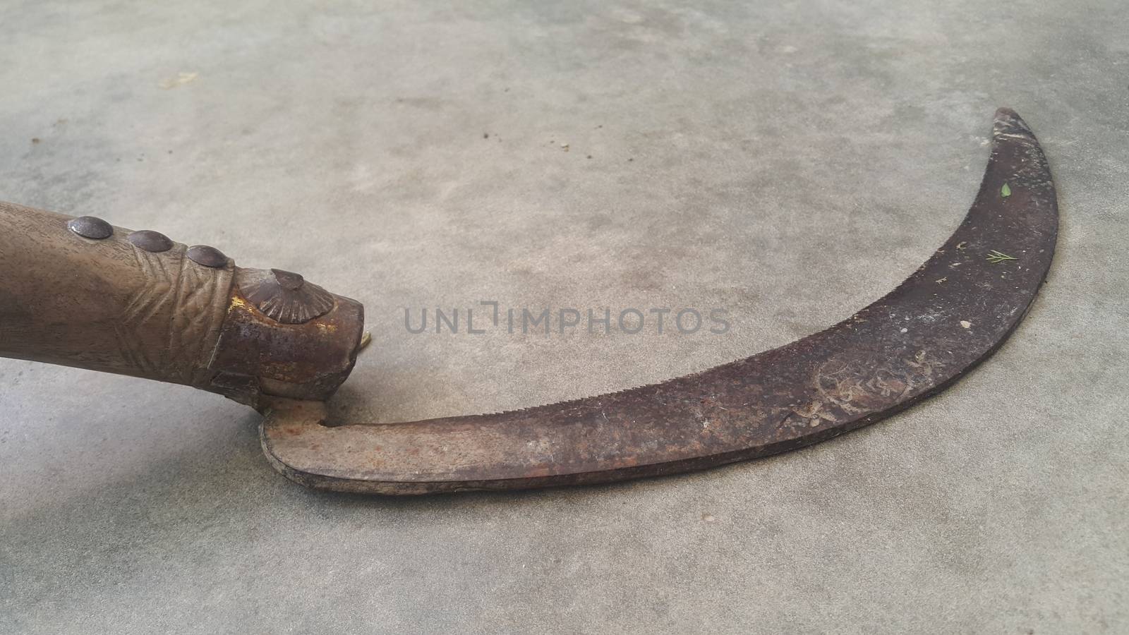 Close-up view of an old sickle (bagging hook or reaping-hook) on the concrete surface. Traditional hand-held agricultural tool.