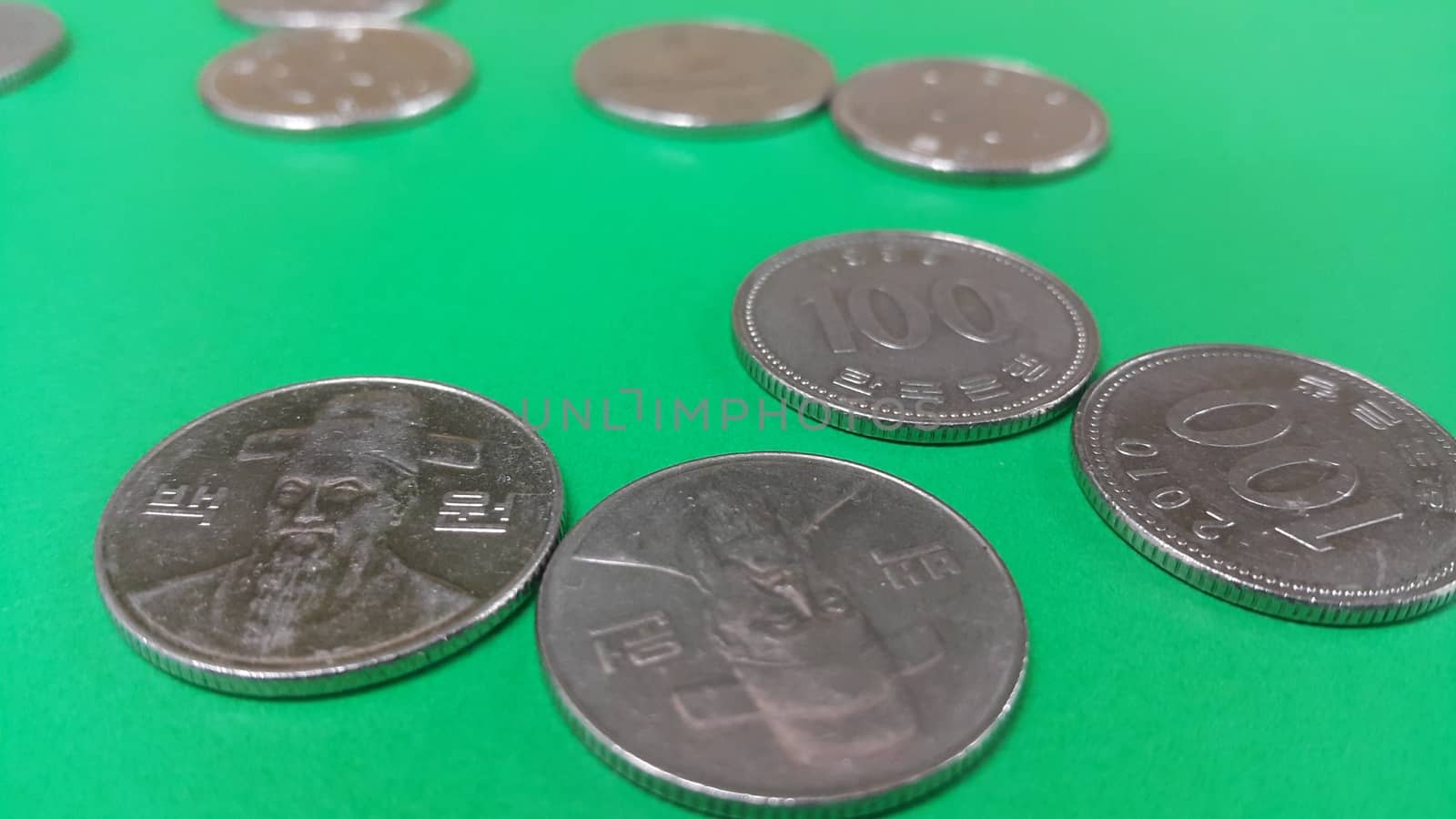 Silver shining Korean won coin scattered over a green floor.
