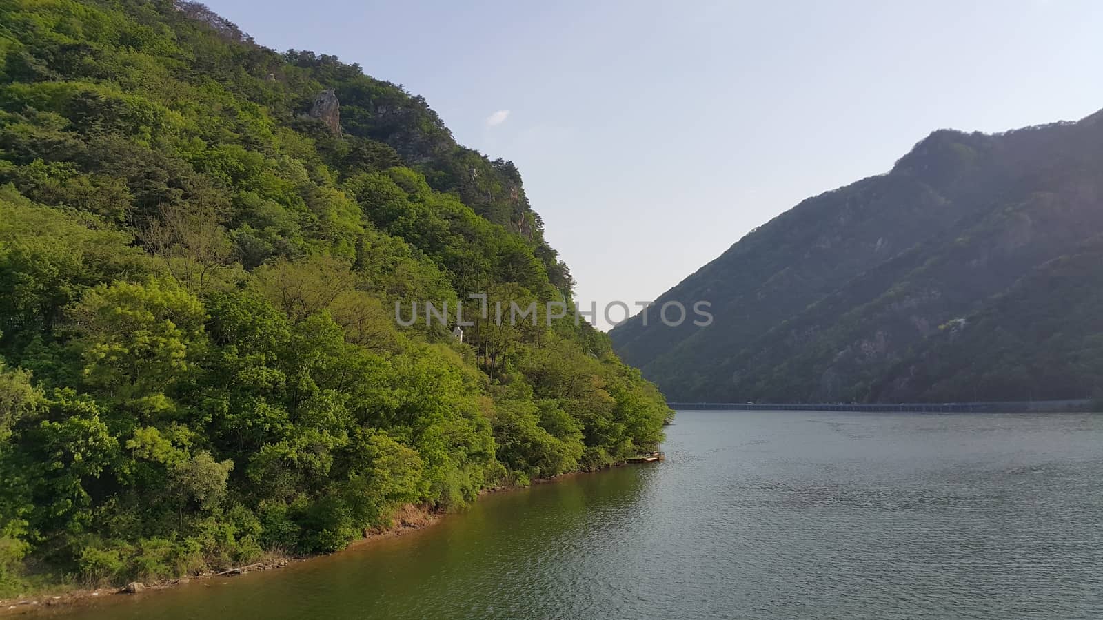 View of beautiful scene of river water and green trees on large hills on a sunny day with blue sky in background. A lovely landscape with breathtaking view over the horizon .