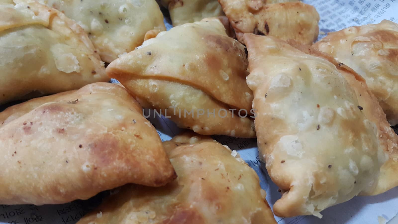 Closeup of delicious home made spicy and crunchy samosa pastries placed in a white ceramic plate on wooden floor
